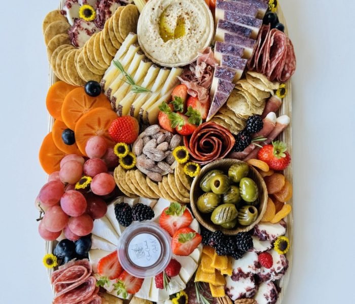 The Grand Graze charcuterie board with 4‑5 cheeses, 3‑4 meats, dried and fresh fruits, olives, pickles, hummus, vegetables, crackers, preserve or jam, chocolate and nuts on a 12×22” bamboo tray — $200 menu item from Shawna Cheeseboards in Reno NV